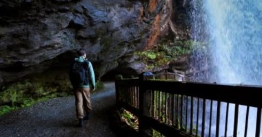 Kuzey Carolina 'daki Nantahala Ulusal Ormanı' ndaki Dry Falls şelalesinin arkasındaki patikada yürüyen turist Appalachian Dağları 'ndaki doğal şelalenin arkasındaki patikada.