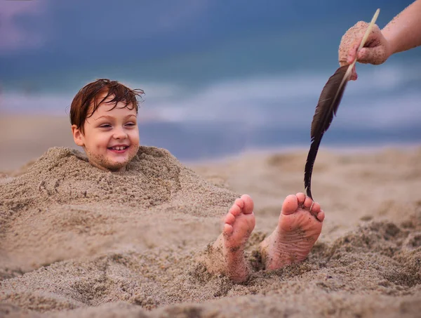 tickling kid\'s feet in a sand. family having fun on sandy beach. summer activity. coastal vacation