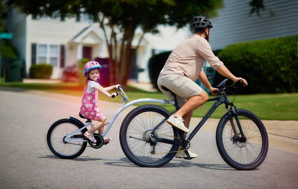 father and daughter, young kid cycling together. bicycle with towable bike trailer. active lifestyle for family with kids