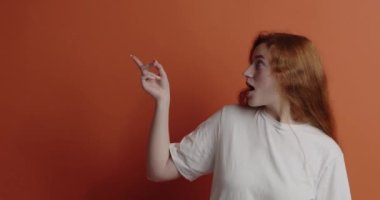 Şaşırmış bir kadın işaret ediyor. Neşeli genç kızıl kız boş fotokopi alanını işaret ediyor. Güzel bir kadın şoke olmuş, turuncu üzerine izole edilmiş. Reklam kavramı 