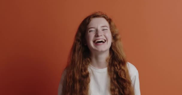ジンジャー女性がカメラを笑っている 積極的な女の子のスウェットシャツを着て誠実に笑みを浮かべて カメラを見て 幸せな気分 オレンジの背景に隔離された屋内スタジオショット — ストック動画