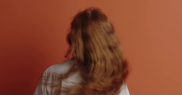 髪の長い幸せな女の子はオレンジの背景に隔離された髪を振って 美しい柔らかい10代の少女の肖像画カメラに向ける ライフスタイルの概念 — ストック動画