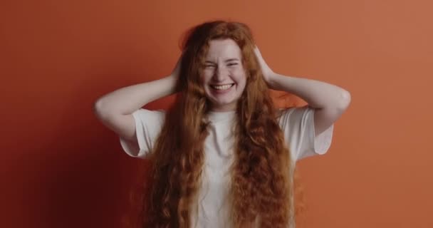 笑う女性は幸せを感じている 積極的な若い女性が大声で ユーモラスな冗談で 髪を振って面白がって笑う オレンジの背景に隔離された屋内スタジオショット — ストック動画