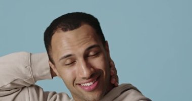 Gülen adam güzellik gösterisinden sonra kafaya dokunuyor. Mutlu adam mavi arka planda izole edilmiş bir resim görüyor. Kendine güvenen kişi kozmetoloji tedavisinden sonra eğleniyor. Yüz bakımı kavramı 