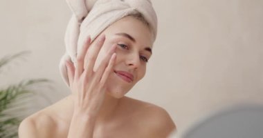 Gülümseyen kadın nemlendirici sürüyor. Gülen, yarı çıplak, yüz kremi süren ve evde aynaya bakan güzel kadının güzel portresini kapat. 