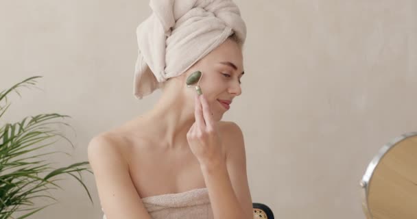 フェイスマッサージ タオル頭の女性は自宅でスキンケア 美容治療のための玉顔マッサージを使用しています 鏡を見てシャワー後マッサージをする女の子 — ストック動画