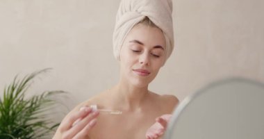 Kadın yüzüne serum döküyor. Avrupalı bir kız yüzüne pipetten serum kolajen nemlendirici sürüyor. Pozitif güzel kadın. Yüz bakımı kavramı 