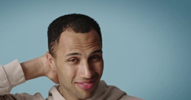 Güzellik gösterisinden sonra kameraya poz veren mutlu adam. Gülümseyen adam mavi arka planda izole edilmiş portreye dokunuyor. Kendine güvenen kişi kozmetoloji tedavisinden sonra eğleniyor. Yüz bakımı kavramı 