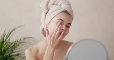 Gülümseyen kadın nemlendirici sürüyor. Gülen, yarı çıplak, yüz kremi süren ve evde aynaya bakan güzel kadının güzel portresini kapat. 