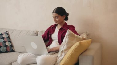 İşi için araştırma yapan genç bir kadın. Gülümseyen Hintli kadın kanepeye oturmuş online alışveriş sitesine göz gezdiriyordu. Evde boş zamanlarında internette gezinen mutlu kız 