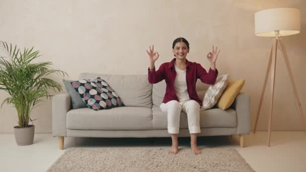 Młoda Dziewczyna Siedzi Kanapie Domu Uśmiechnięta Szczęśliwy Pozytywny Pokazując Gest — Wideo stockowe