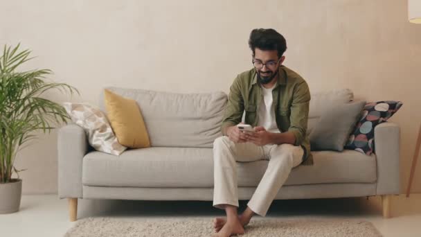 Sorrindo Homem Milenar Sentar Sofá Casa Divertir Usando Gadget Celular — Vídeo de Stock