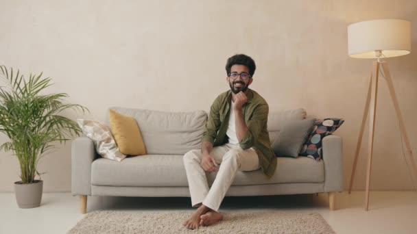Bonito Homem Indiano Positivo Posando Câmera Enquanto Sentado Sofá Interior — Vídeo de Stock