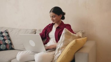 İşi için araştırma yapan genç bir kadın. Gülümseyen Hintli kadın kanepeye oturmuş online alışveriş sitesine göz gezdiriyordu. Evde boş zamanlarında internette gezinen mutlu kız 