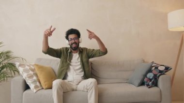 Beyaz kulaklıklı heyecanlı Hintli adam oturmuş müzikten zevk alıyor. Mutlu adam rahat bir yerde favori şarkıyı dinliyor. 