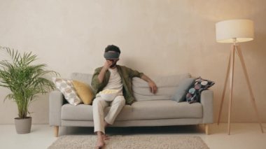 Genç Hintli adam VR kulaklık takıyor ve oturma odasında patlamış mısırla film izliyor. Kıvırcık adam evde patlamış mısır yiyen sanal gerçeklik gözlüğü kullanarak film izliyor. 