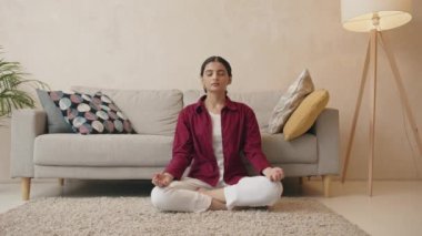 Oturma odasında yoga yapan rahat Hintli kadının tüm vücut portresi. Meditasyon ve spor konsepti 