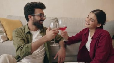 Kanepenin yanında oturan mutlu Hintli çift ellerinde kırmızı şarap kadehleri ve evde romantik bir randevu geçirirken tıkırdıyorlar. 