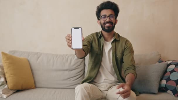 在家里用手机笑着的印度年轻人 快乐的家伙展示智能手机屏幕 指指点点空白显示 — 图库视频影像