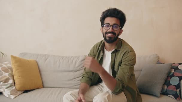 Усміхнений Молодий Бородатий Чоловік Сидить Дивані Дивлячись Камеру Щасливий Індійський — стокове відео