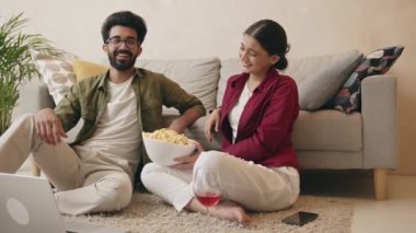 Mutlu Hintli çift yerde oturuyor, rahat bir günde dizüstü bilgisayar kullanıyor, film ya da TV şovu izliyor, patlamış mısır yiyor, kaynaşıyor, evde dinleniyorlar.