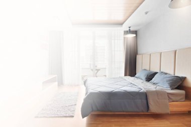 Yatak odasında rahat bir yatak, beyaz ışık arka planı, temizlik ve hijyen anlayışı var.