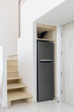 Minimalist, modern bir evde geniş bir alan yaratmak için merdiven altına yerleştirilmiş parlak bir buzdolabı. Bu tasarım, merdiven altı depolama ve etkin aygıt yerleştirme akıllıca kullanımını gösterir.