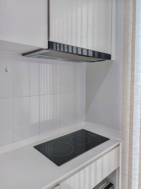 Modern mutfak tasarımı, siyah cam yüzeyi ve dahili egzoz kapağı olan parlak bir elektrikli ocak içeriyor. Minimalist ve temiz, küçük alanlar ve çağdaş iç mekanlar için mükemmel..