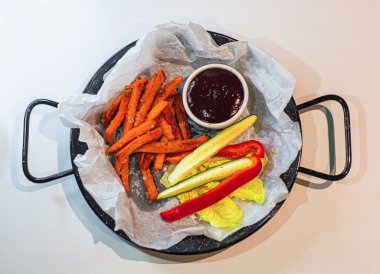 Siyah tabak patates kızartması, taze sebze ve sos..