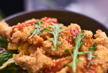 Fried chicken in breadcrumbs with tomato sauce and salad greens on black plate in cafe