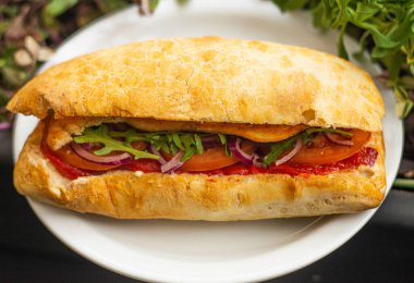 Large ciabatta sandwich with salad, fresh vegetables and onions, and meat.