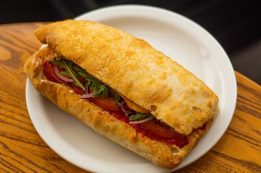 Large ciabatta sandwich with salad, fresh vegetables and onions, and meat.