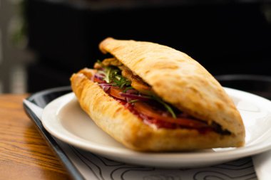 Large ciabatta sandwich with salad, fresh vegetables and onions, and meat.