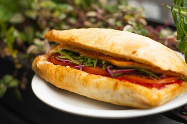 Large ciabatta sandwich with salad, fresh vegetables and onions, and meat.