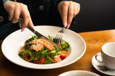 White ceramic plate of fresh salad with salmon, vegetables, tomatoes and arugula with sesame seeds.
