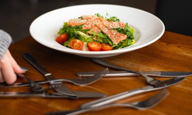 White ceramic plate of fresh salad with salmon, vegetables, tomatoes and arugula with sesame seeds.