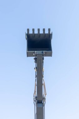 Toprak hareket eden makinenin kolu ve kovası mavi gökyüzünde izole edilmiş.