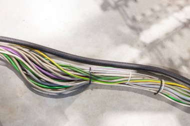 Beton bir yüzey üzerinde esnek kanallarla kaplanmış çok renkli elektrik kabloları düzgünce paketlenmiş.