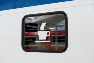Tren penceresindeki kahve fincanı sembolü gündüz vakti istasyon peronunu yansıtıyor.