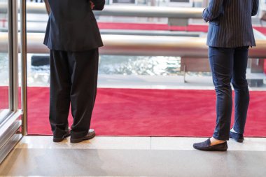 İki kişi resmi bir etkinlik sırasında çeşmenin yanında kırmızı halıda dikiliyorlar.