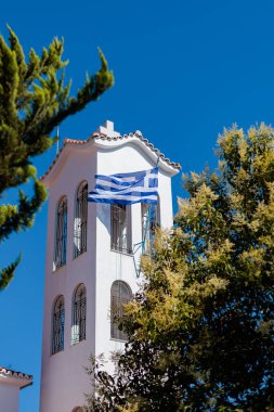 Güneşli havada beyaz bir kilise kulesinde dalgalanan Yunan bayrağı