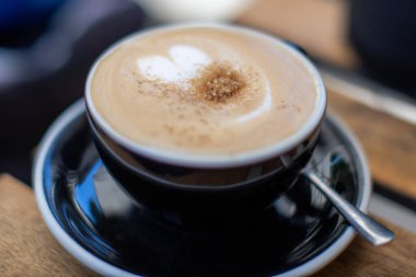 Sabah saatlerinde sıcak bir kafede üzerine tarçın serpilmiş siyah bir fincanda kremalı latte.