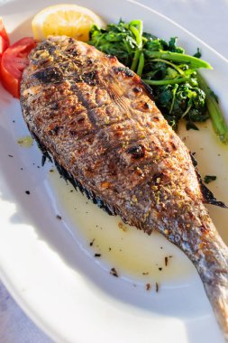 Gün batımında deniz kenarındaki bir restoranda taze sebze ve limonla servis edilen ızgara deniz kabuğu.