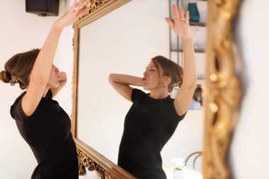 Büyük bir aynanın önünde kendinden emin bir şekilde dans eden kadın şık bir ortamda kendini ifade ediyor.