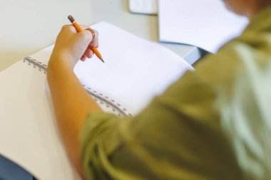 Samimi bir ofis ortamında boş sayfalara turuncu kalemle notlar yazan biri.