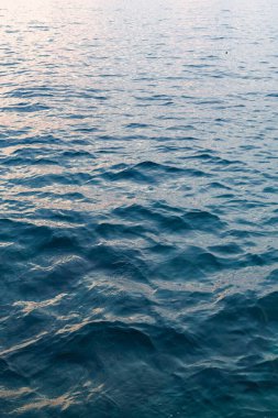 Sakin bir akşamda, gün batımının yumuşak renklerini yansıtan sakin dalgalar yavaşça kıyıya vurur.