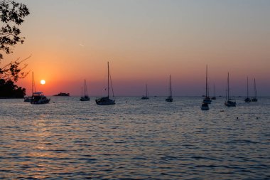Sahil kenarındaki teknelerle dolu sakin bir limanda gün batımı.