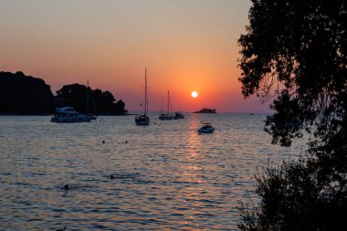 Sahil kenarındaki teknelerle dolu sakin bir limanda gün batımı.