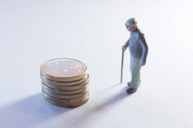 Yığılmış madeni paraların yanında duran yaşlı kişi, yaşlanmayla ilgili ekonomik kaygıları gösteriyor