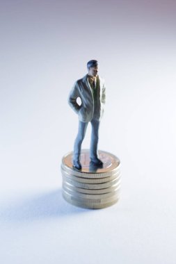 Minyatür figür, madeni başarının resimli bir temsili olarak dolar banknotlarıyla çevrili madeni paraların üzerinde duruyor.